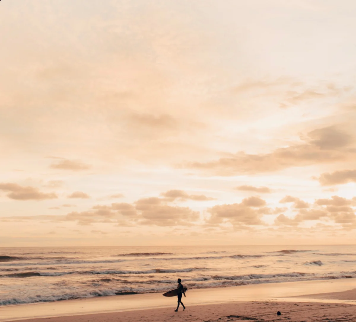 A surfer walking a vast beach at first light